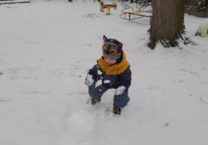 Dziecko toczy kulę śnieżną w ogrodzie przedszkolnym